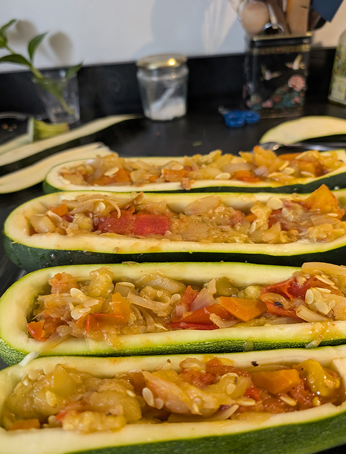 Courgettes rondes et longues évidées, garnies d'une farce aux légumes, préparées pour une cuisson au four dans le cadre d'un batch cooking.