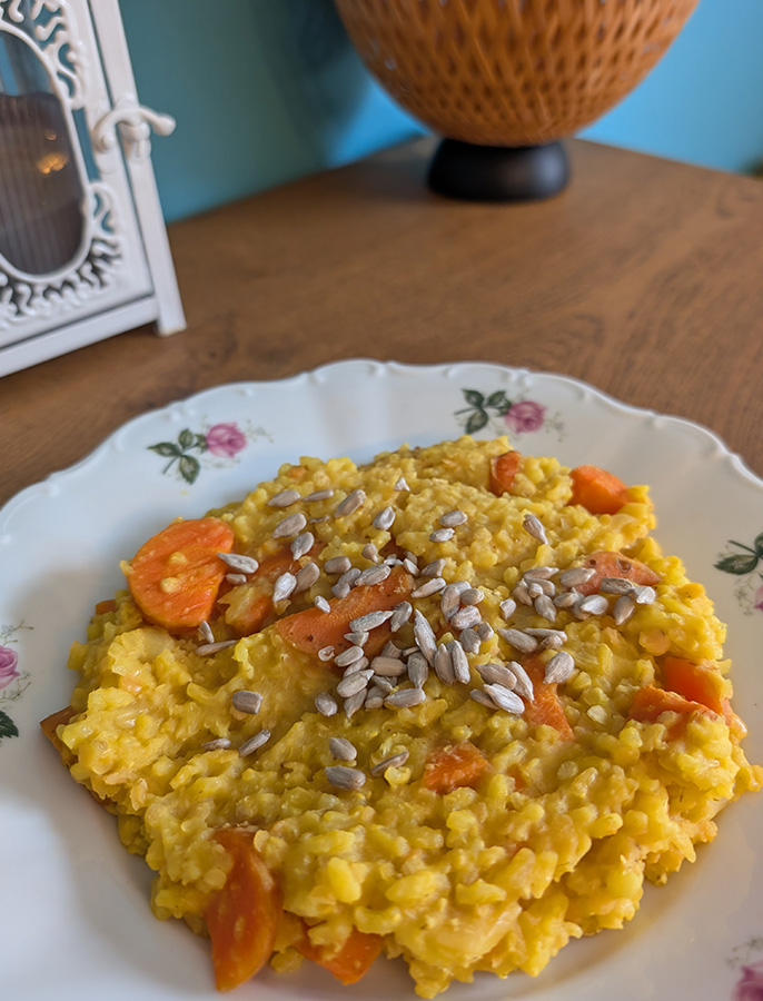 Assiette de risotto crémeux aux carottes parfumé au curcuma, garni de graines de tournesol, préparé en batch cooking.